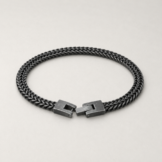 A dark gunmetal braided chain bracelet with a matching geometric slide clasp, displayed on a light gray background.